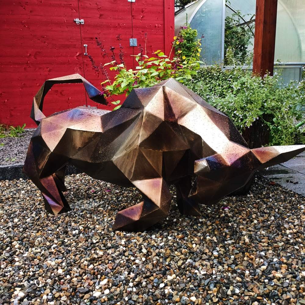 Fierce polygonal bull sculpture crafted from dark welded steel, set on a gravel background
